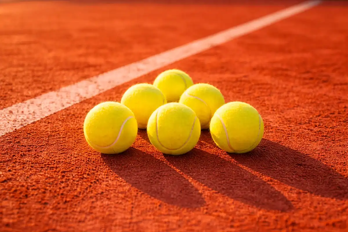 Mehrere Tennisbälle auf rotem Sandplatz in einer symmetrischen Anordnung